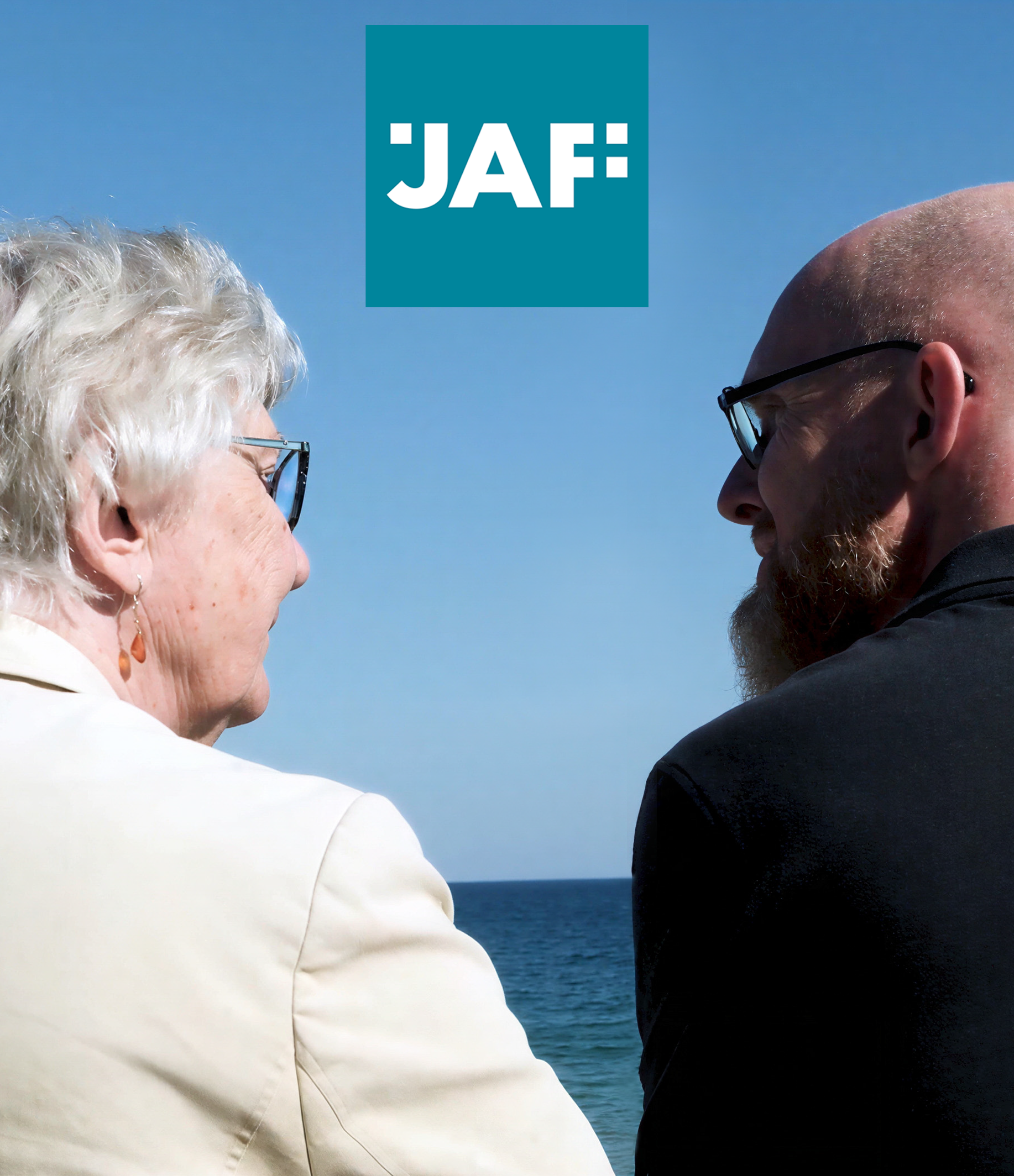 A man and a woman sit alongside each other facing out to the sea. They are pictured not quite in profile. The JAF logo is in the middle of the picture.