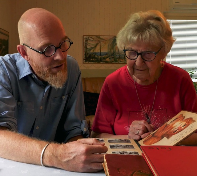 A man and a woman sitting together by a table and looking at a photo album.